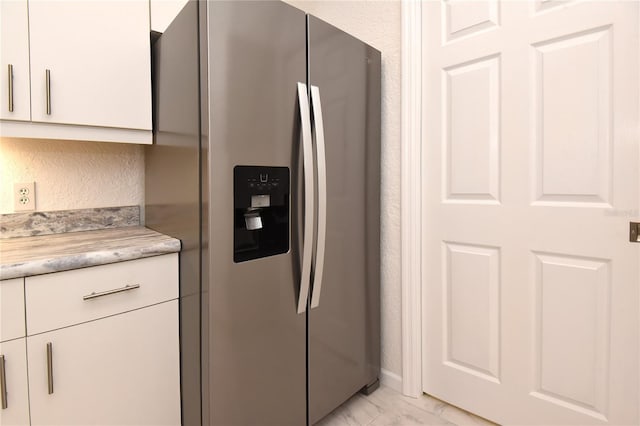 kitchen featuring stainless steel fridge with ice dispenser, light countertops, white cabinetry, a textured wall, and marble finish floor