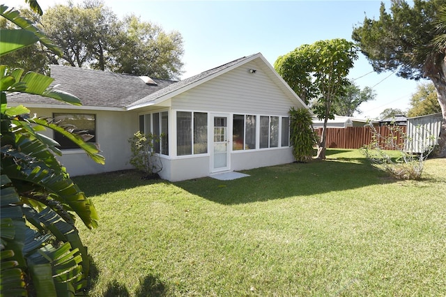 back of house featuring fence, a yard, a sunroom, a shingled roof, and stucco siding