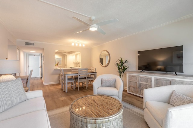 living area featuring wood finished floors, visible vents, arched walkways, ornamental molding, and ceiling fan