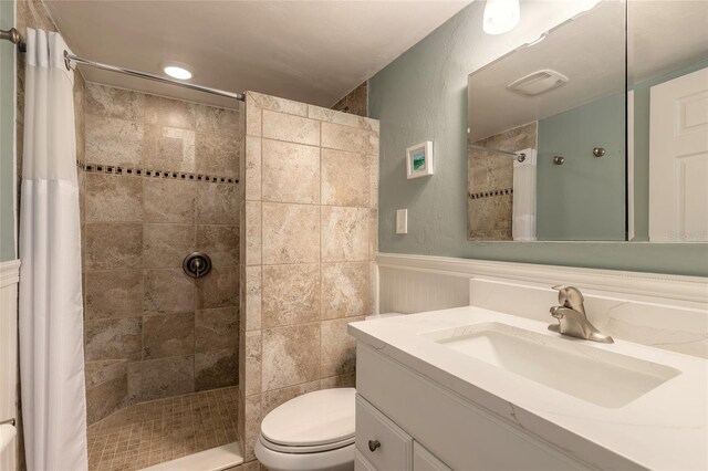 full bath with visible vents, toilet, a tile shower, wainscoting, and vanity