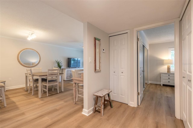 hall featuring baseboards, light wood-type flooring, and ornamental molding