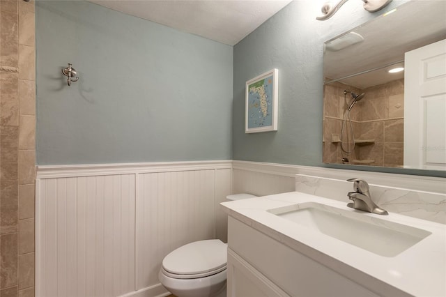 bathroom featuring vanity, toilet, a wainscoted wall, and tiled shower