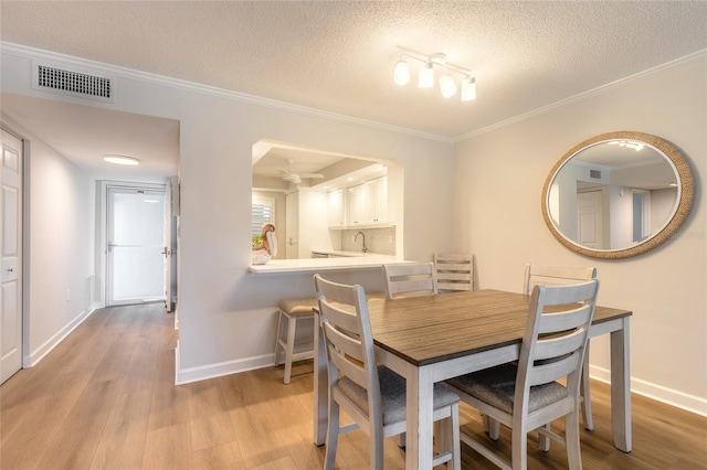 dining area with baseboards, visible vents, light wood-style flooring, a textured ceiling, and crown molding