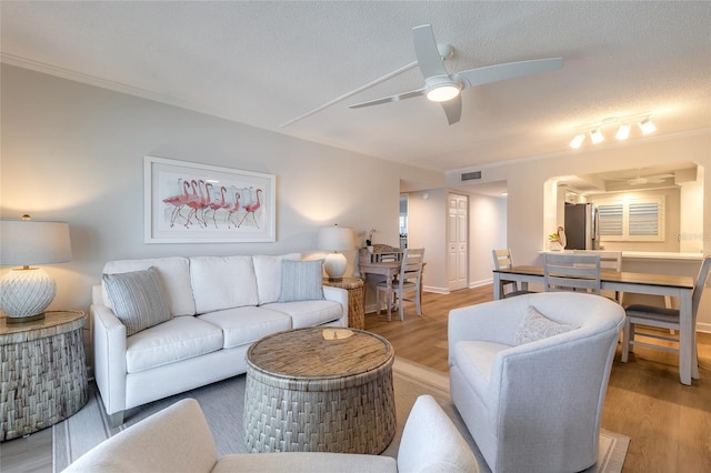 living room with a textured ceiling, ceiling fan, crown molding, and light wood finished floors