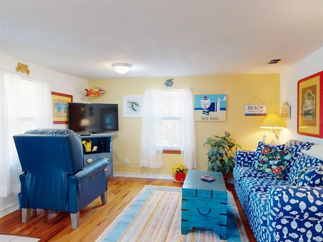 living area featuring visible vents, plenty of natural light, baseboards, and wood finished floors