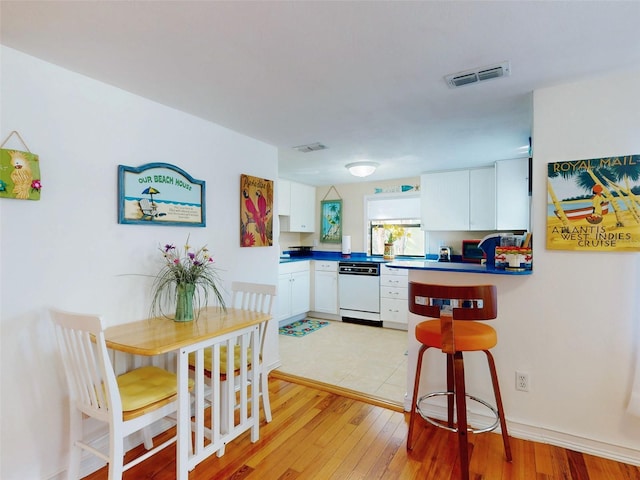 kitchen with dark countertops, white cabinets, visible vents, and white dishwasher