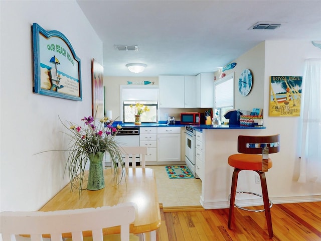 kitchen with visible vents, white appliances, white cabinetry, and light wood-style floors