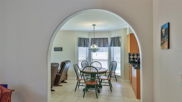 dining room featuring arched walkways, a notable chandelier, baseboards, and light tile patterned floors