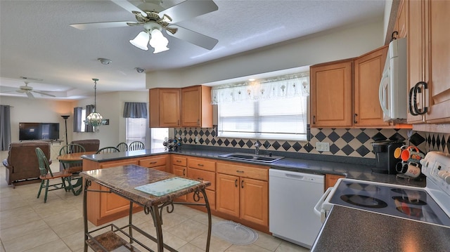 kitchen with a sink, backsplash, dark countertops, white appliances, and ceiling fan