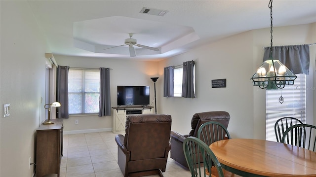 dining area with visible vents, baseboards, ceiling fan with notable chandelier, light tile patterned flooring, and a raised ceiling