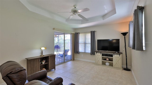 living room featuring light tile patterned floors, baseboards, a raised ceiling, and ceiling fan