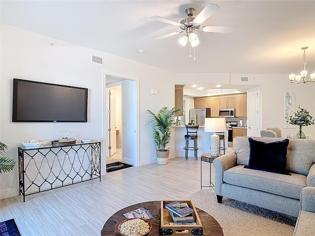 living area with baseboards, ceiling fan with notable chandelier, visible vents, and light wood-type flooring