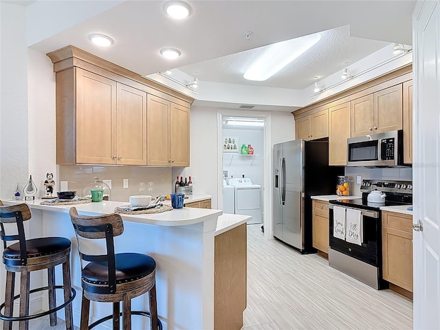 kitchen with stainless steel appliances, a peninsula, and light brown cabinets