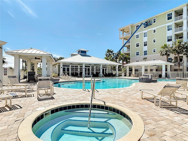 community pool with a patio area, a hot tub, and fence