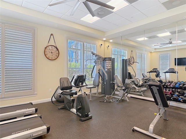 workout area with a paneled ceiling, baseboards, a raised ceiling, and ceiling fan