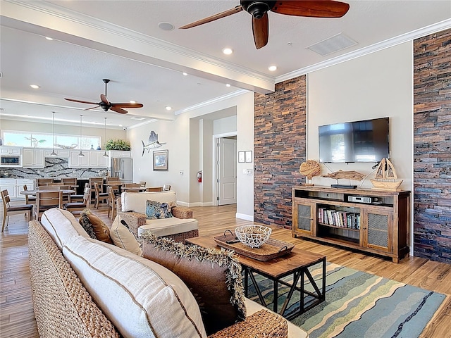 living room with light wood-type flooring, visible vents, ornamental molding, baseboards, and ceiling fan