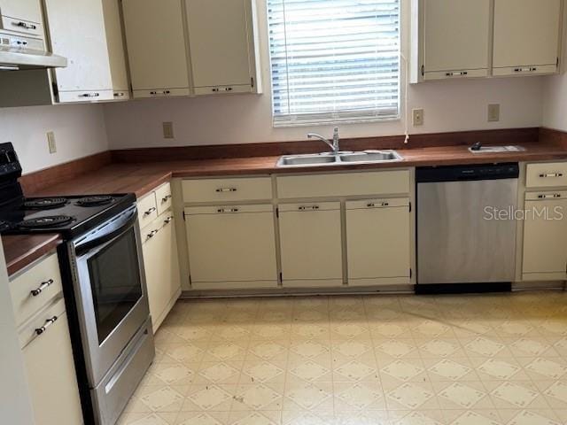 kitchen featuring stainless steel dishwasher, dark countertops, a sink, light floors, and electric range oven