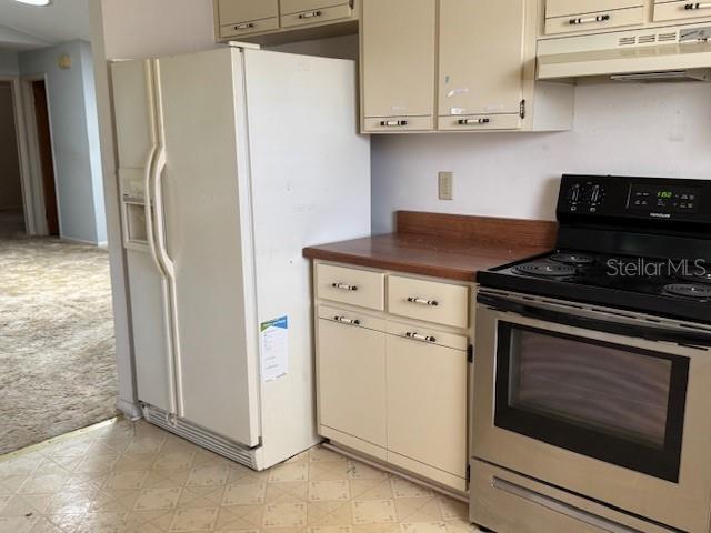 kitchen with cream cabinetry, under cabinet range hood, electric stove, white refrigerator with ice dispenser, and light colored carpet