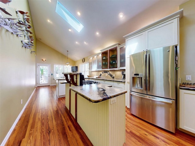 536 Faulkner St, New Smyrna Beach, FL 32168 - kitchen with stainless steel fridge, a kitchen island, a skylight, light wood finished floors, and glass insert cabinets