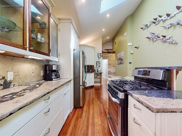 536 Faulkner St, New Smyrna Beach, FL 32168 - kitchen with backsplash, light wood finished floors, light stone countertops, appliances with stainless steel finishes, and lofted ceiling with skylight