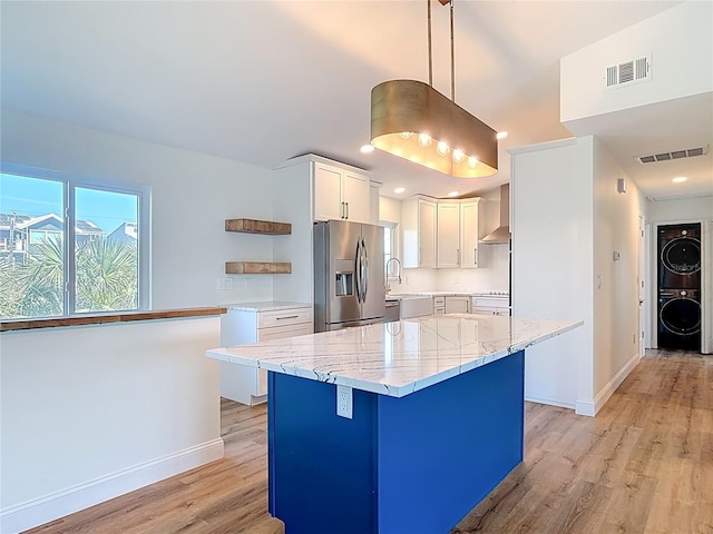 6937 Turtlemound Rd, New Smyrna Beach, FL 32169 - kitchen with stainless steel fridge with ice dispenser, stacked washer / drying machine, light wood-style flooring, white cabinetry, and a center island