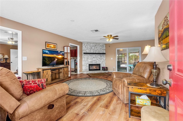 living room with a stone fireplace, visible vents, wood finished floors, and ceiling fan