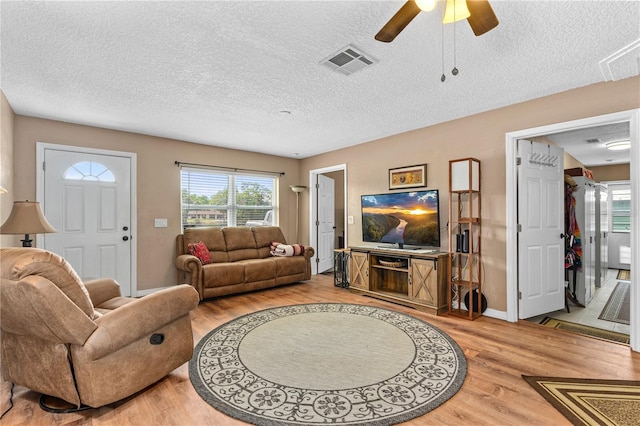 living room featuring a textured ceiling, visible vents, light wood finished floors, baseboards, and ceiling fan