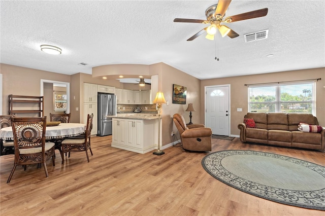 living room featuring a ceiling fan, a textured ceiling, light wood-style flooring, baseboards, and visible vents