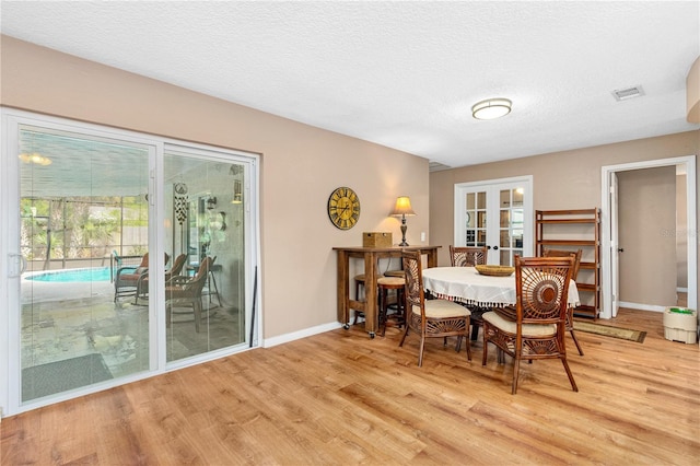 dining room with visible vents, light wood-style floors, french doors, and a textured ceiling