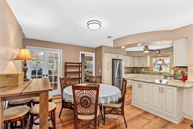 dining area featuring french doors, light wood finished floors, a textured ceiling, visible vents, and ceiling fan