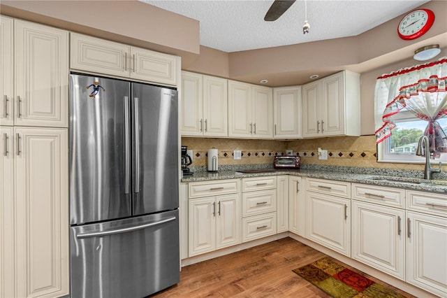 kitchen featuring light stone counters, a sink, freestanding refrigerator, light wood-style flooring, and decorative backsplash