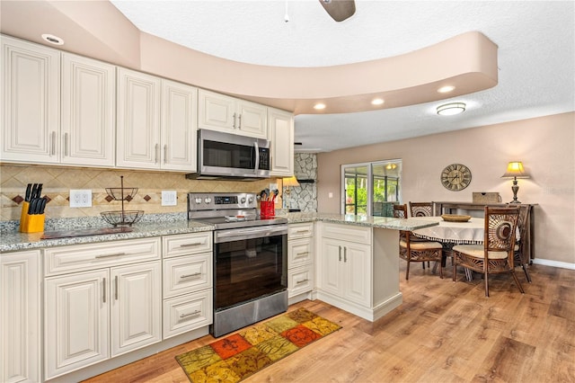 kitchen featuring backsplash, light wood finished floors, appliances with stainless steel finishes, a peninsula, and white cabinets