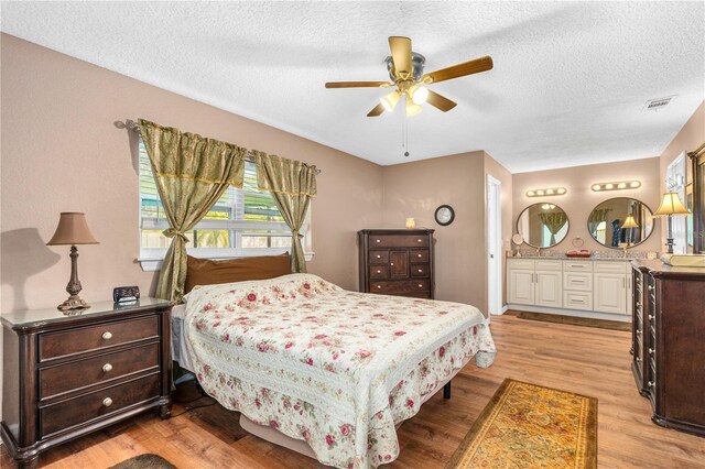 bedroom with ensuite bathroom, a textured ceiling, visible vents, ceiling fan, and light wood-style floors