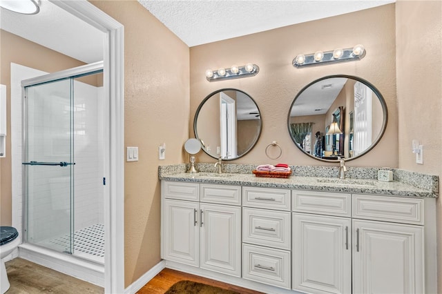 bathroom featuring double vanity, a sink, a stall shower, and wood finished floors