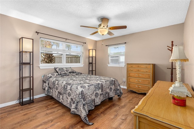 bedroom with baseboards, cooling unit, wood finished floors, and a textured ceiling
