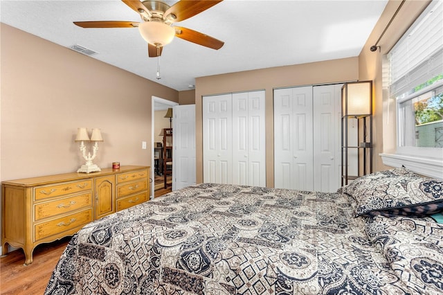 bedroom featuring multiple closets, ceiling fan, visible vents, and light wood-style floors