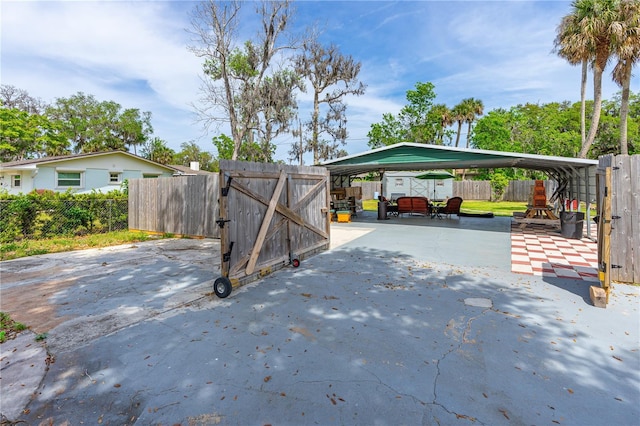 view of parking with driveway, a gate, fence, and a detached carport
