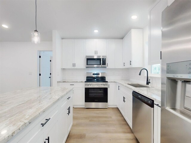 kitchen with light stone counters, a sink, light wood finished floors, appliances with stainless steel finishes, and decorative backsplash