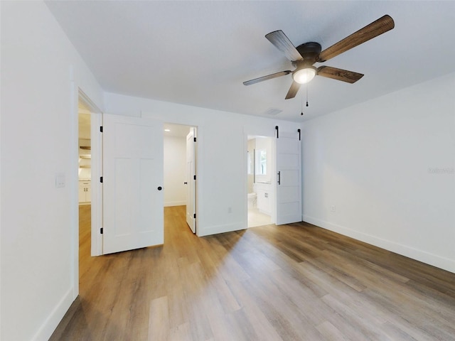 unfurnished bedroom featuring baseboards, ensuite bath, visible vents, ceiling fan, and wood finished floors