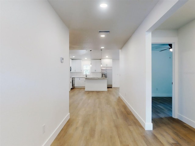 hallway featuring recessed lighting, baseboards, a sink, light wood finished floors, and visible vents