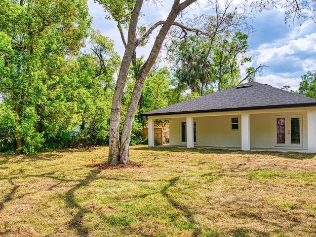 rear view of house with a shingled roof, a lawn, stucco siding, and french doors