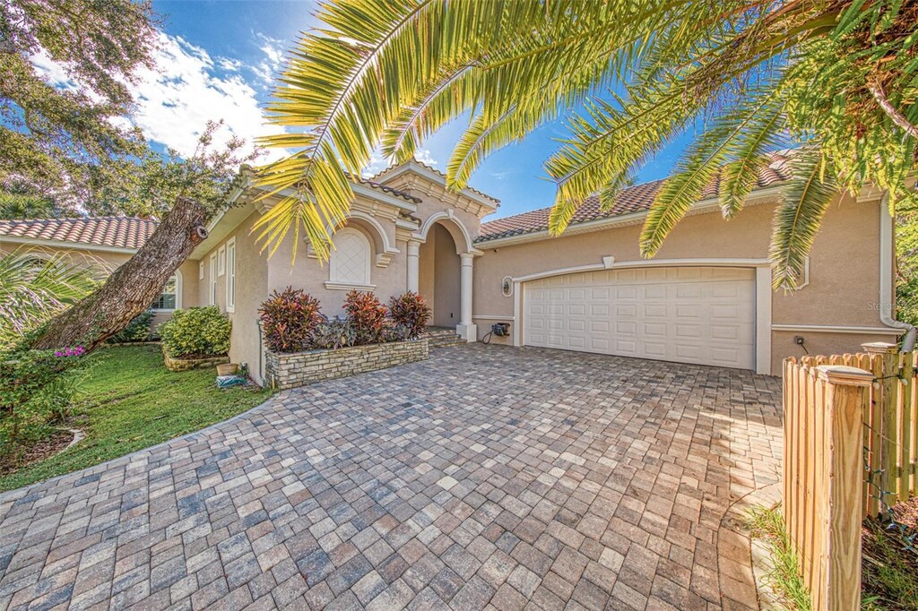 mediterranean / spanish house with a tile roof, decorative driveway, stucco siding, and an attached garage