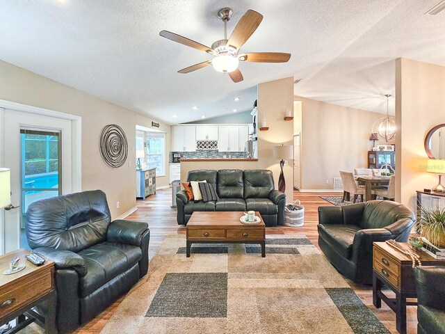 living room with light wood-style floors, ceiling fan with notable chandelier, vaulted ceiling, and a textured ceiling