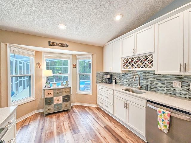 kitchen with tasteful backsplash, white cabinetry, light wood-style floors, stainless steel dishwasher, and a sink