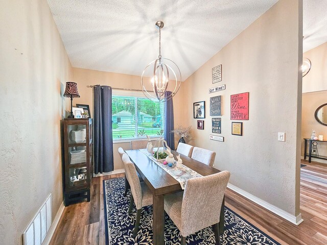 dining space with a notable chandelier, a textured ceiling, visible vents, lofted ceiling, and wood finished floors
