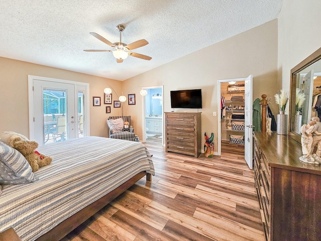bedroom with a spacious closet, light wood-type flooring, connected bathroom, vaulted ceiling, and access to exterior