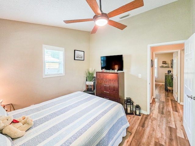 bedroom featuring baseboards, light wood-style flooring, a textured ceiling, visible vents, and ceiling fan