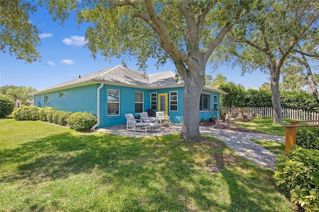 rear view of property featuring a patio area, stucco siding, fence, and a lawn