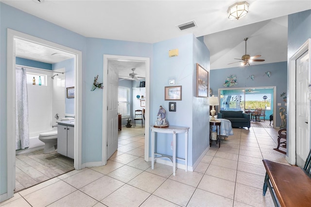hallway with lofted ceiling, baseboards, visible vents, and light tile patterned floors