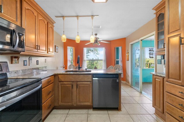kitchen featuring a peninsula, a sink, glass insert cabinets, brown cabinets, and appliances with stainless steel finishes